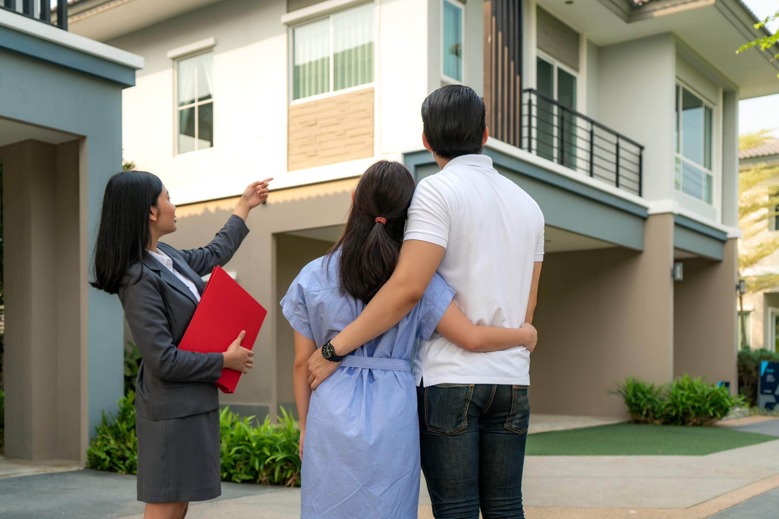 Asian woman Real estate broker agent showing a house project detail in her file to the young Asian couple lover looking and interest to buy it. Buying a new house.